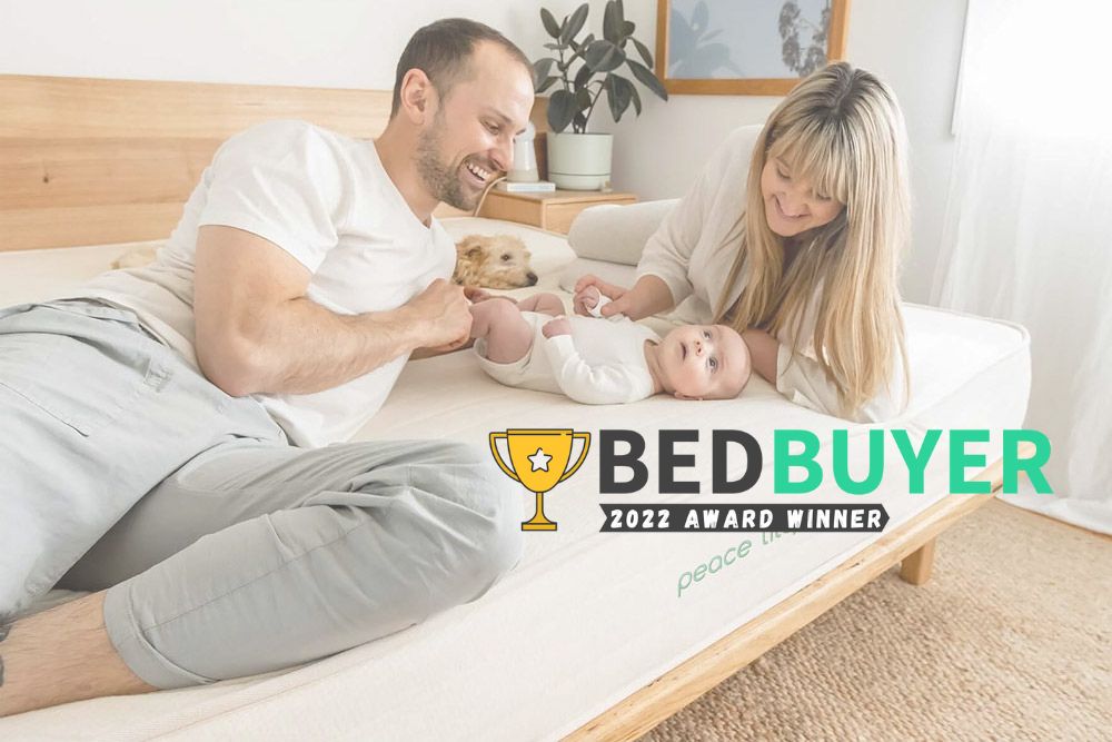 The image shows two young parents resting on a bed with their baby, with the caption Bedbuyer 2022 award winner. 