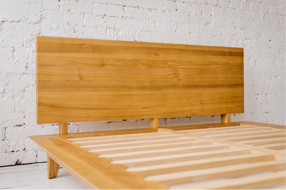 Close-up of the Peace Lily timber bed frame's solid ash headboard and slatted base against a white brick wall